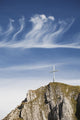Mountain Peak With A Cross On Top Against A Blue Sky With Clouds Wall Mural