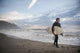 A Young Man Carries His Surfboard Down The Beach Wall Mural