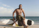A Man Sits On His Surfboard On The Beach Wall Mural