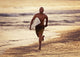 A Man Runs On The Wet Beach At Sunset With His Surfboard Wall Mural