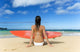 Hawaii, Kauai, Woman Sitting On Beach With Surfboard, View From Behind Wall Mural