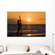 Female Surfer On Beach Silhouetted Against Orange Sunset Over Ocean Wall Mural