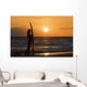 Female Surfer On Beach Silhouetted Against Orange Sunset Over Ocean Wall Mural