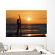 Female Surfer On Beach Silhouetted Against Orange Sunset Over Ocean Wall Mural