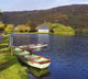 St Finbarre's Oratory And Rowing Boats On Shore Of Gougane Barra Lake Wall Mural