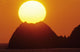 Sun Setting In Orange Sky Over Ocean And Silhouetted Hill Wall Mural