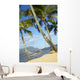 Hammock tied between palm trees on sandy beach Wall Mural