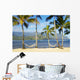 Two hammocks hanging between palm trees on sandy tropical beach Wall Mural