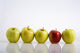 Four Yellow Apples With One Red Apple In A Row On A Reflective Surface Wall Mural