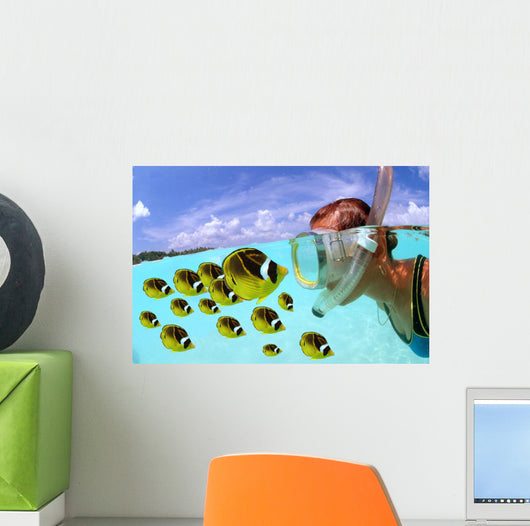 Over/under woman snorkeler face to face with Butterflyfish school Wall Mural