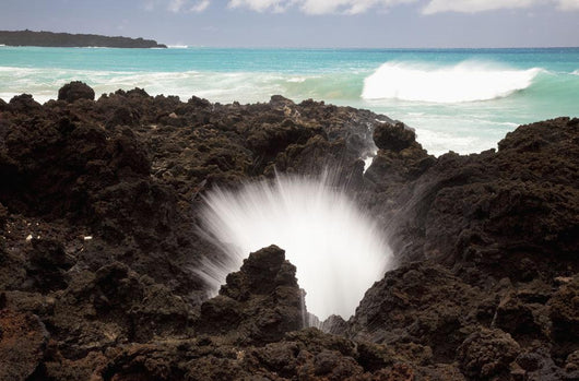 A burst of water through a blowhole in some lava rocks Wall Mural