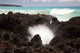 A burst of water through a blowhole in some lava rocks Wall Mural
