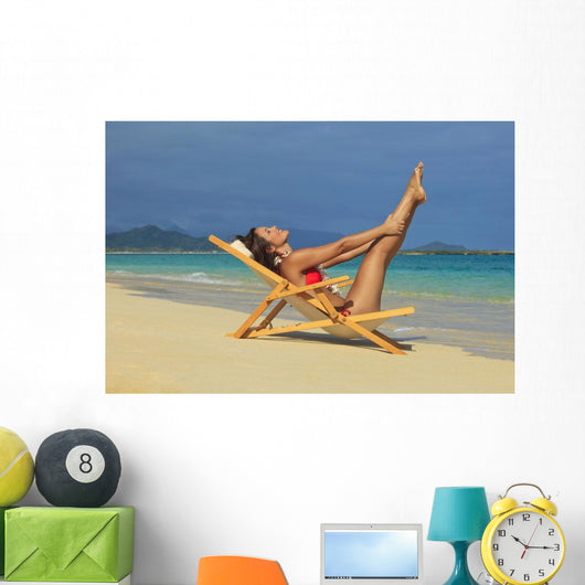 Beautiful woman stretches in a lounge chair on the beach Wall Mural