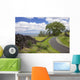A stone wall lines a country road with views of Maui in the background Wall Mural