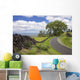 A stone wall lines a country road with views of Maui in the background Wall Mural