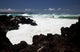 A wave breaks with lave rocks in the foreground Wall Mural