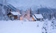 Two Snowcovered Homes In A Wintry Meadow At Dawn With Inside Lights On Wall Mural