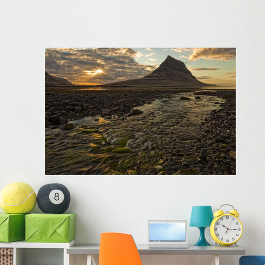 The mountain Kirkjufell rises above the ocean as the sun sets Wall Mural