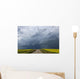 Storm clouds gather over a sunlit canola field and road Wall Mural