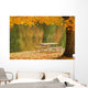 A picnic table beside a tranquil lake with golden leaves on the trees Wall Mural