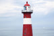 Red and white lighthouse along the coast with a sailboat Wall Mural