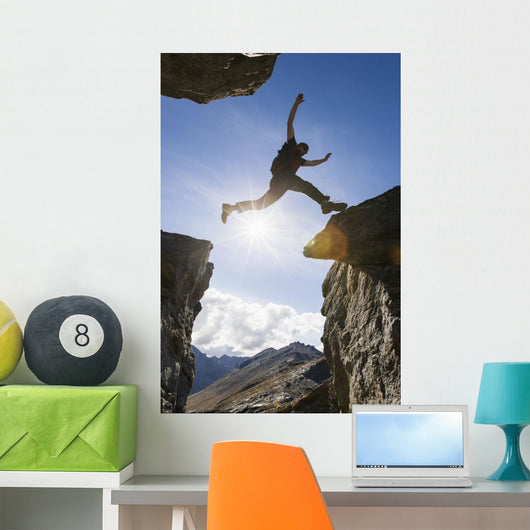 Backlit View Of Hiker Leaping Between Rocks Near Noatak River Wall Mural