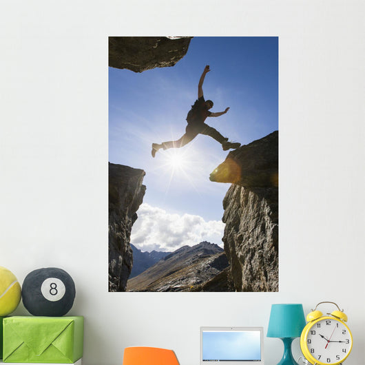 Backlit View Of Hiker Leaping Between Rocks Near Noatak River Wall Mural