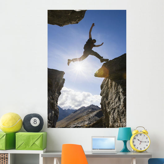 Backlit View Of Hiker Leaping Between Rocks Near Noatak River Wall Mural