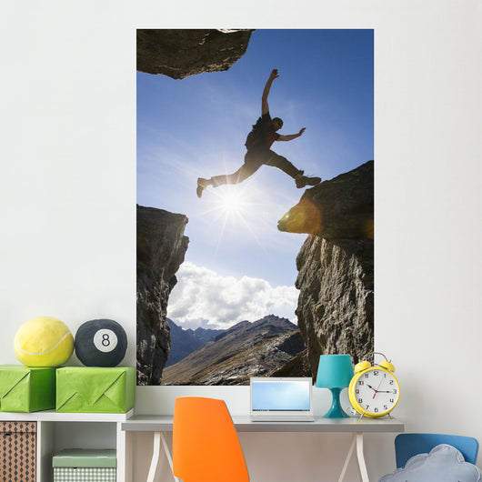 Backlit View Of Hiker Leaping Between Rocks Near Noatak River Wall Mural