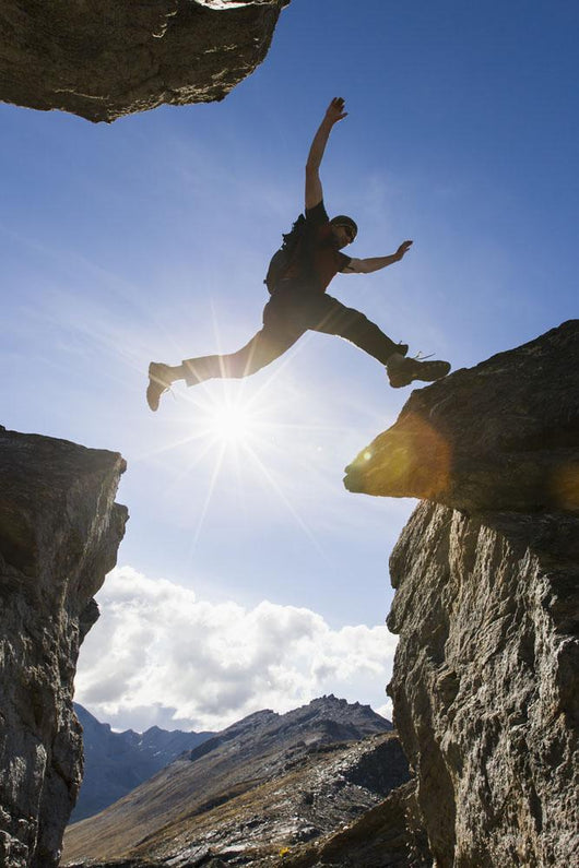 Backlit View Of Hiker Leaping Between Rocks Near Noatak River Wall Mural