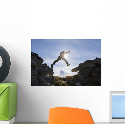 Backlit View Of Hiker Leaping Between Rocks Near Noatak River Wall Mural