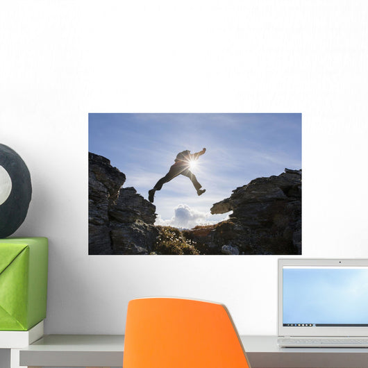 Backlit View Of Hiker Leaping Between Rocks Near Noatak River Wall Mural