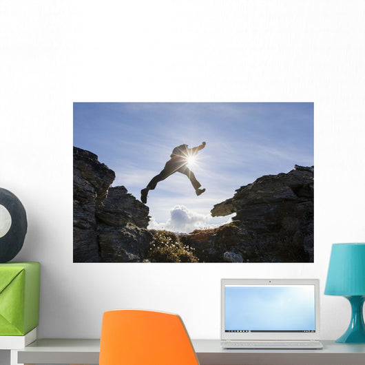 Backlit View Of Hiker Leaping Between Rocks Near Noatak River Wall Mural