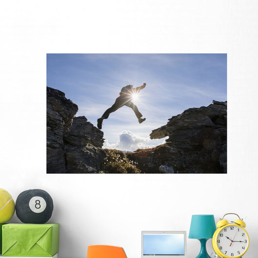 Backlit View Of Hiker Leaping Between Rocks Near Noatak River Wall Mural