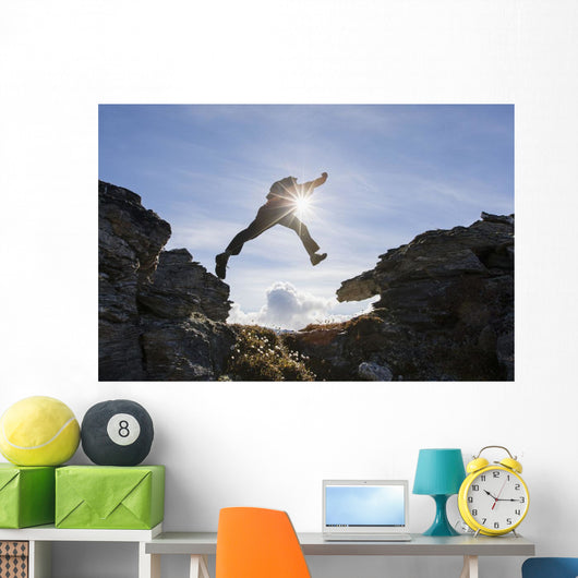 Backlit View Of Hiker Leaping Between Rocks Near Noatak River Wall Mural