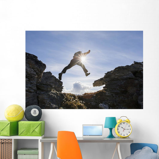 Backlit View Of Hiker Leaping Between Rocks Near Noatak River Wall Mural