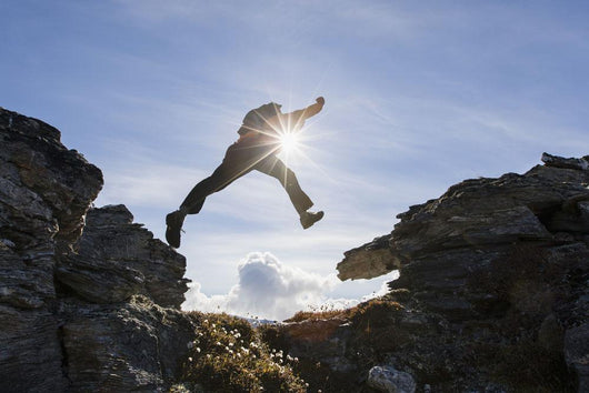 Backlit View Of Hiker Leaping Between Rocks Near Noatak River Wall Mural