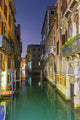 Turquoise water in a narrow canal between buildings at dusk Wall Mural