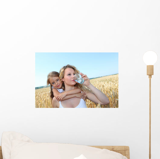Mother drinking water in wheat field with child Wall Mural