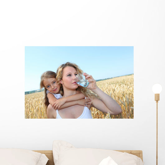 Mother drinking water in wheat field with child Wall Mural