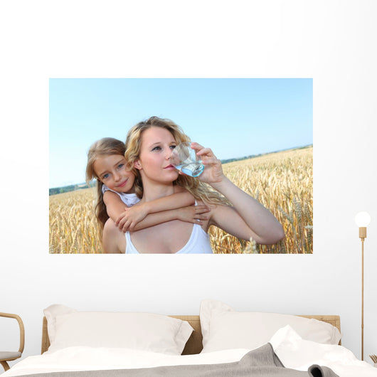 Mother drinking water in wheat field with child Wall Mural