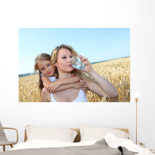 Mother drinking water in wheat field with child Wall Mural