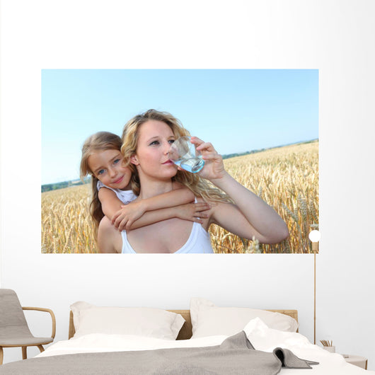 Mother drinking water in wheat field with child Wall Mural