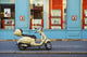 A motorized scooter parked outside a blue building along a street Wall Mural