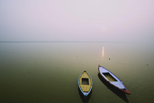 Two wooden boats sit on the tranquil water of the Ganges Wall Mural