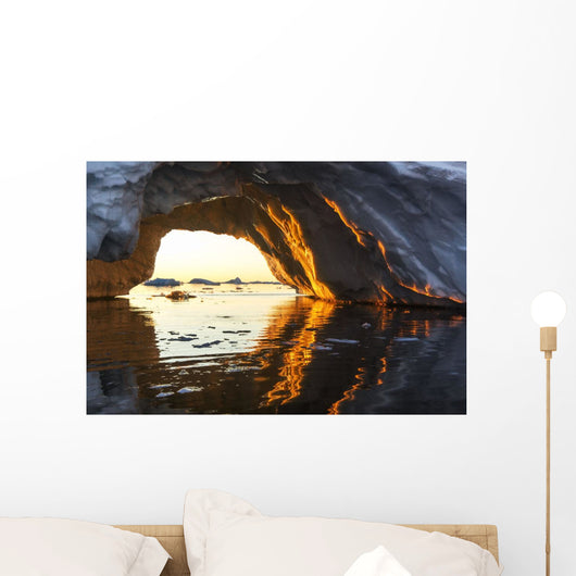 Midnight sun shines through arched iceberg near Lemaire Channel Wall Mural