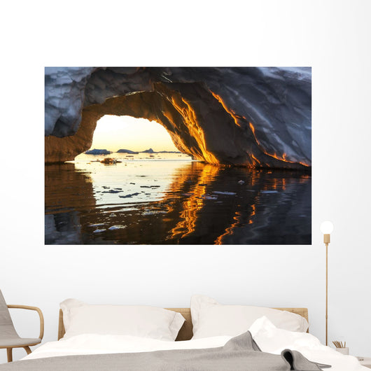 Midnight sun shines through arched iceberg near Lemaire Channel Wall Mural