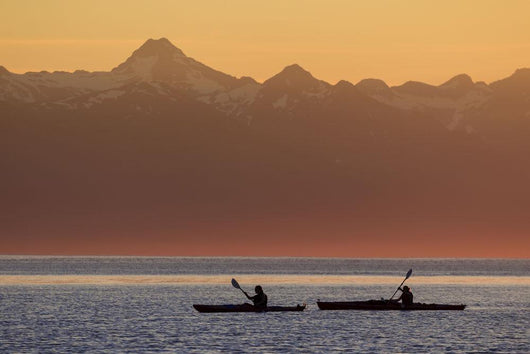 Two female sea kayakers enjoy a warm summer evening while paddling Wall Mural