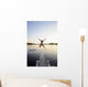 A swimmer jumps off a diving board as the sun sets over a lake Wall Mural
