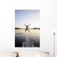 A swimmer jumps off a diving board as the sun sets over a lake Wall Mural